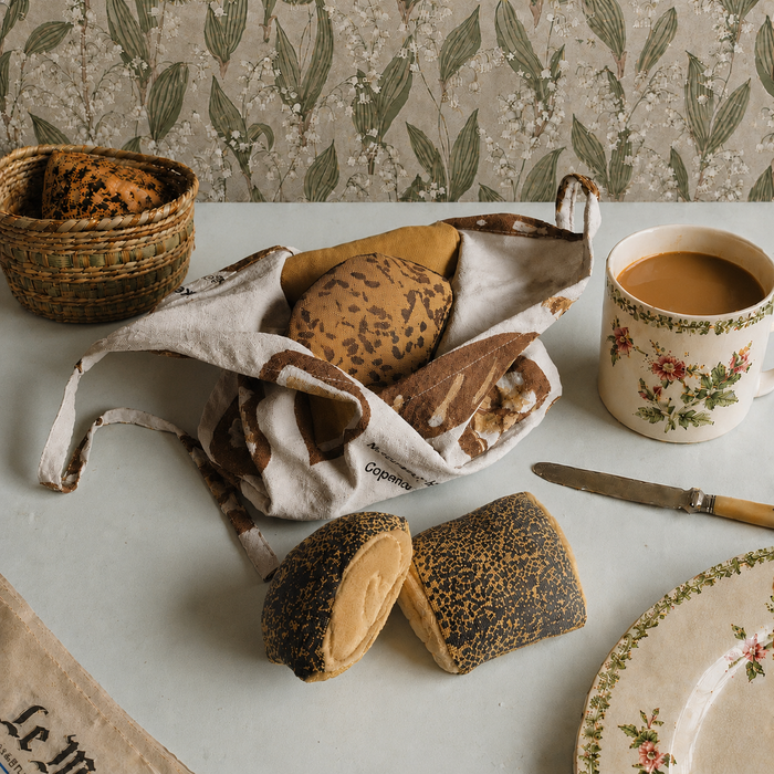 Pretend Baked goods in a basket with a cup of coffee on a table with floral-patterned wallpaper.