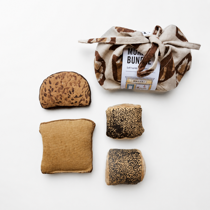 Handmade fabric morning buns set with toast, bread slice, two seeded rolls and a tied cotton storage bag on a white studio background.