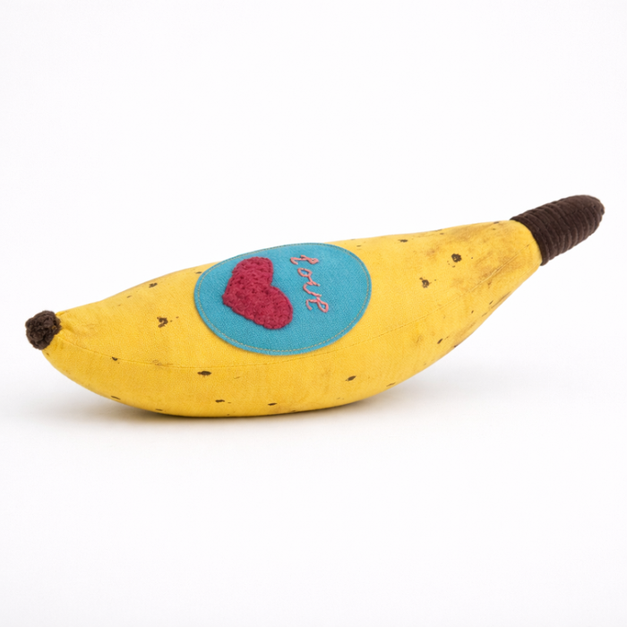 Banana-shaped pillow with a heart and text patch on a white background