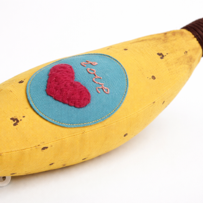 Banana-shaped pillow with a heart and 'love' patch on a white background