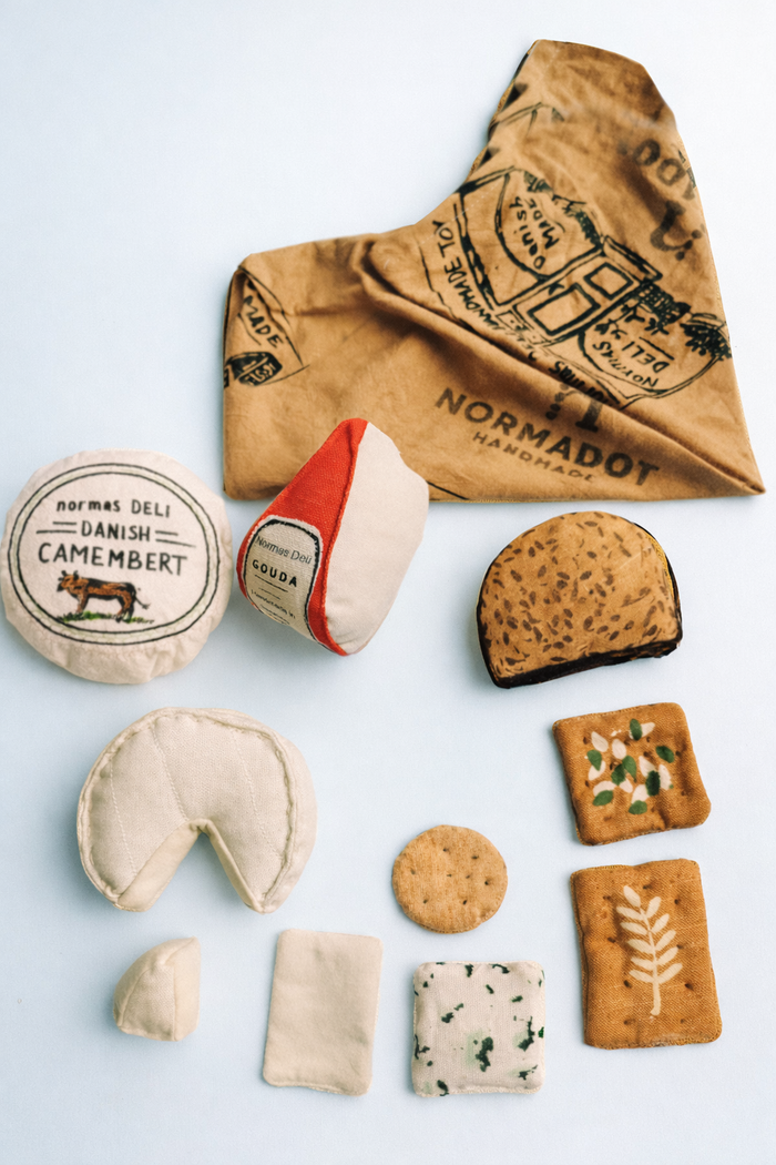 Assorted fabric cheese and cookies with a Normadot bag on a light blue background