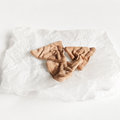 Handmade fabric triangle crackers displayed on crumpled white paper in a light studio product setting. Soft textile pretend play food with hand-printed details and small embroidered seeds.
