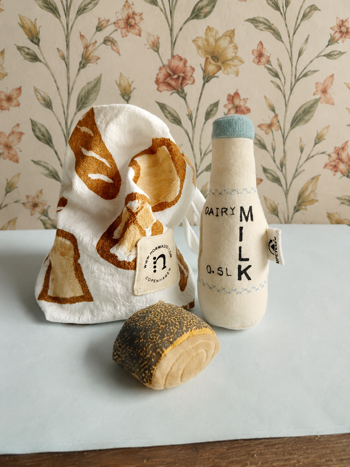 Toy set resembling a bag of bread, a bottle of milk, and a loaf of bread on a floral-patterned background.