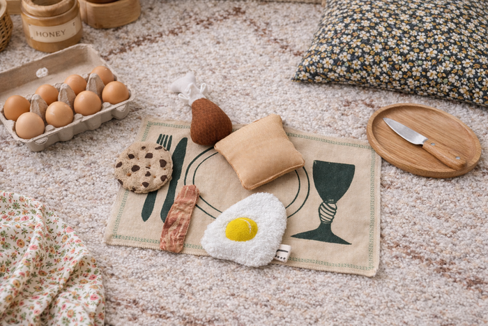Playful arrangement of food-themed toys on a textured surface with a floral pillow.