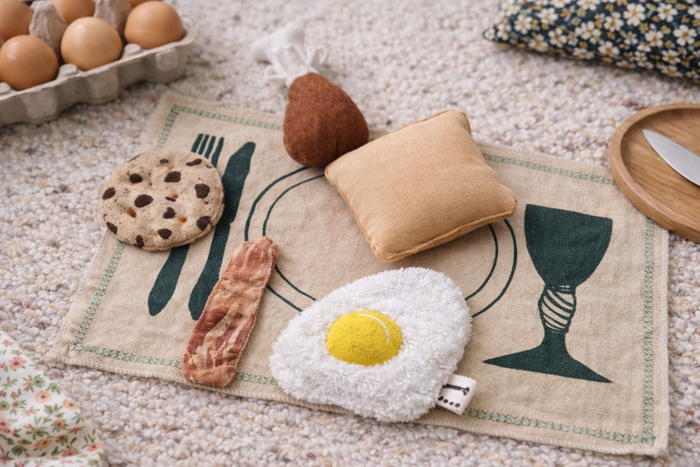 Handmade fabric breakfast play food with egg, bacon, cookie, pear and toast on a printed cotton play mat