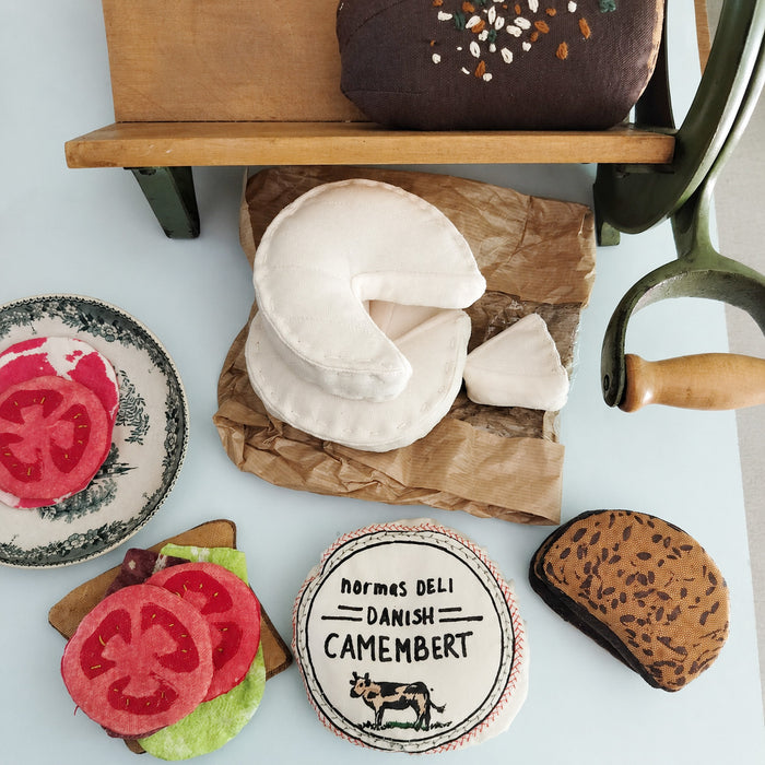 Handmade textile play food deli set with soft fabric camembert cheese, tomato slices, sandwich toppings, rye bread slices and toy bread for pretend play kitchens.