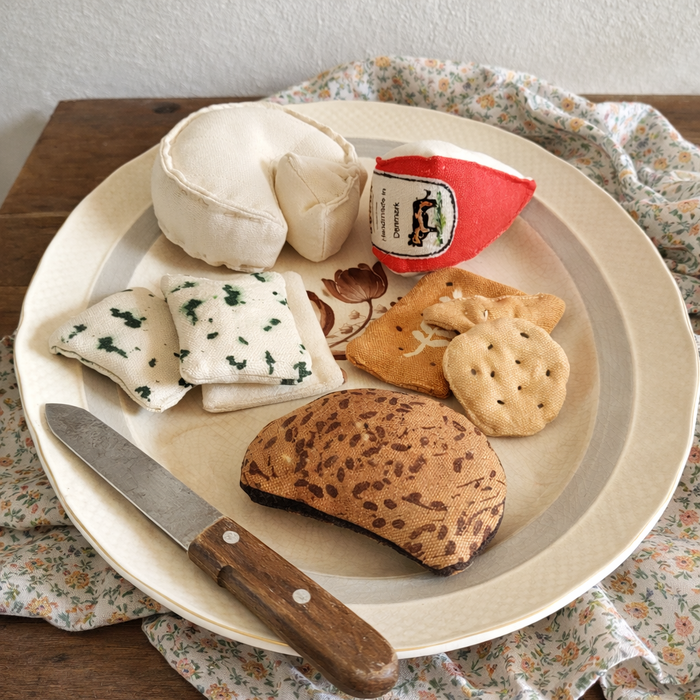 Handmade fabric lunch set with rye bread slice, cheese, crackers and small deli pieces on a plate with a wooden-handled knife.