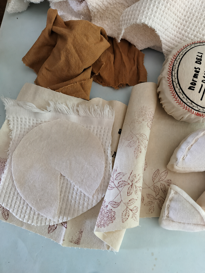 Handmade textile camembert play food in progress with cotton fabric pieces, printed cover, soft cheese wedges and fabric scraps for pretend play toy production.