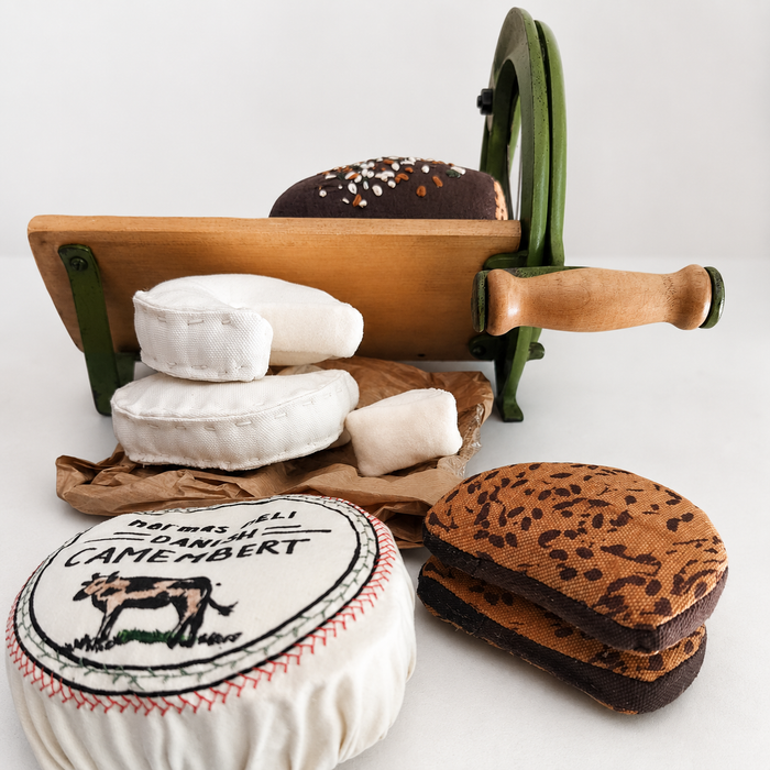 Handmade textile deli play food set with soft camembert cheese, small cheese wedges, rye bread slices and toy bread slicer for pretend play kitchens.