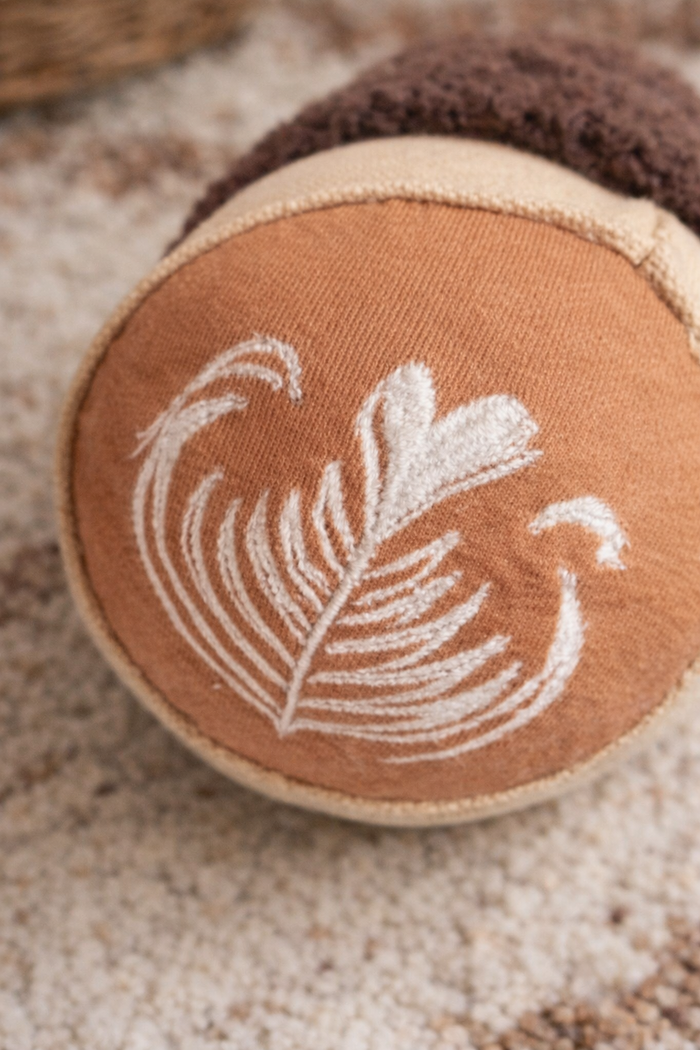 Close-up of handmade cappuccino cup baby rattle with embroidered latte art on soft cotton canvas