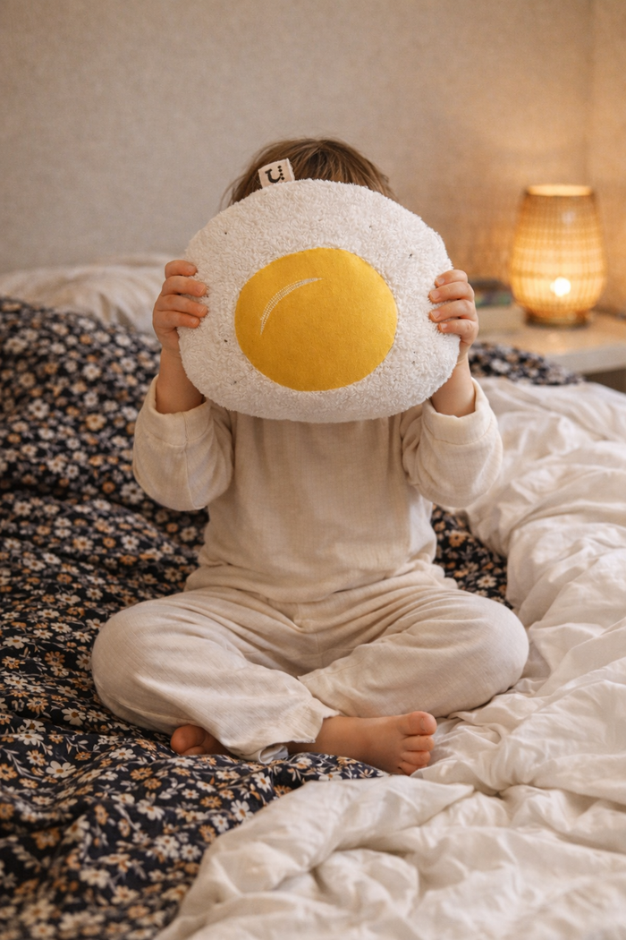 Child holding a fried egg shaped cushion on a bed