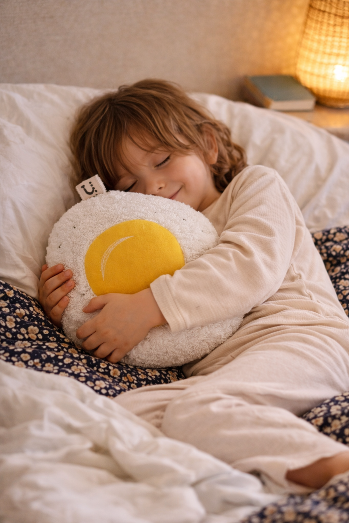 Child sleeping in bed with a plush Fried egg shaped pillow
