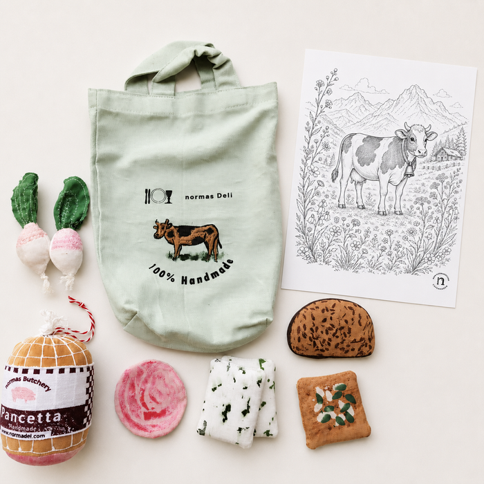 Handmade soft deli grocery play set with fabric pancetta, radishes, bread, blue cheese, seed cracker, cotton tote bag and cow colouring sheet on a light background.