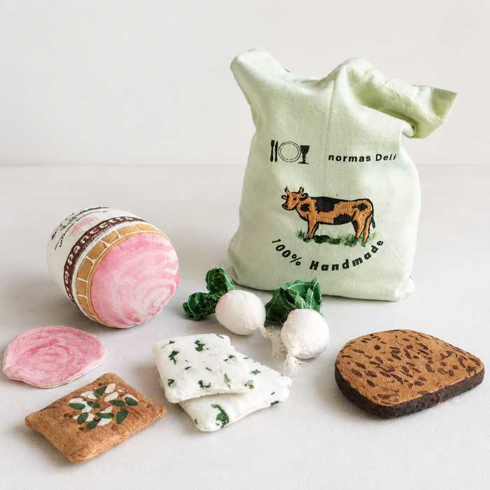 Handmade fabric deli play food set with Pancetta, radishes, crackers, cheese pieces, bread slice and Normas Deli tote bag in a light studio setting.