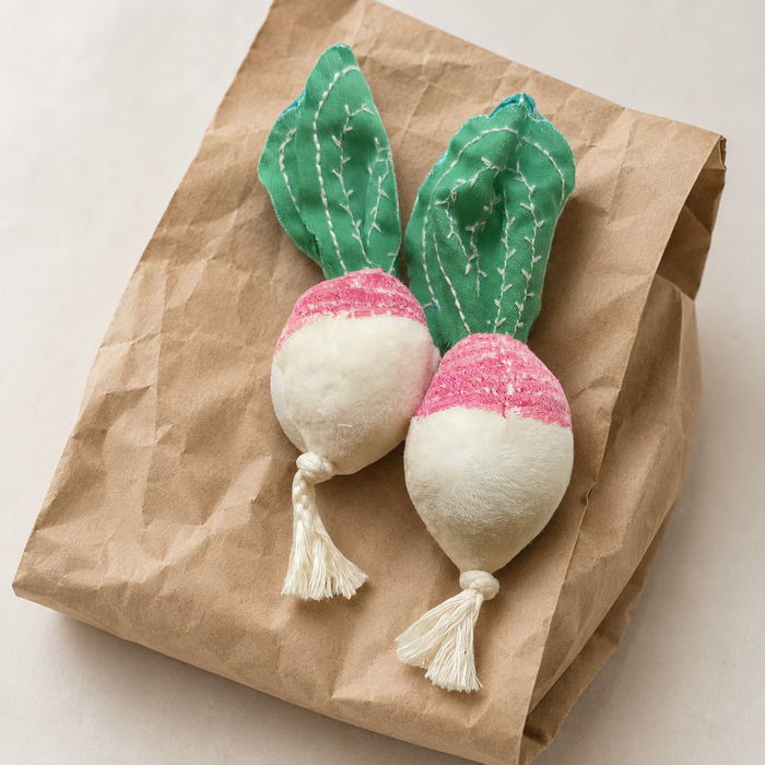 Handmade fabric radishes lying on a flat brown paper gardener bag in a light natural product setting.