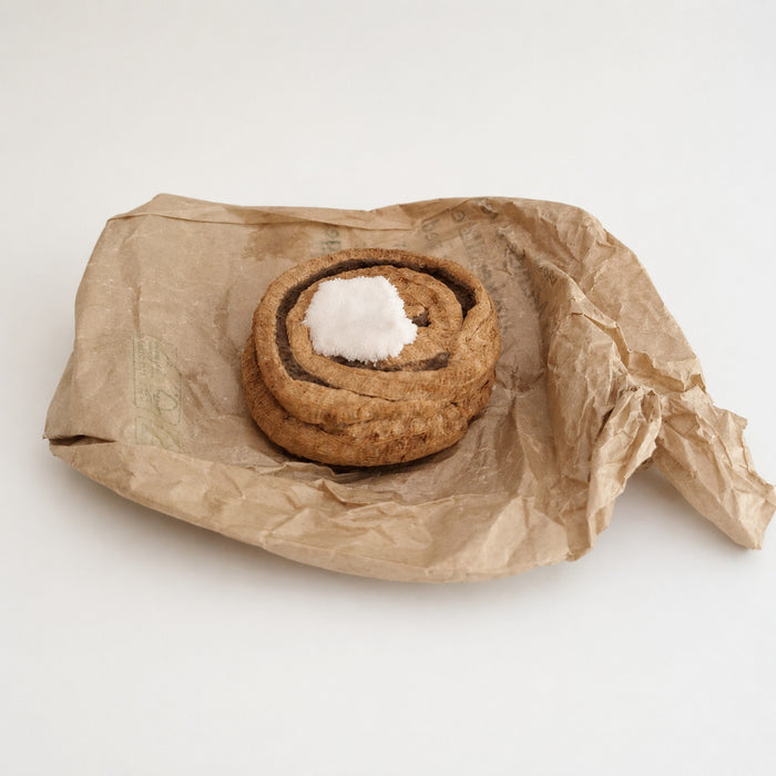 Handmade Danish kanelsnegl fabric play food with soft velour icing, displayed on crumpled brown paper against a light background.