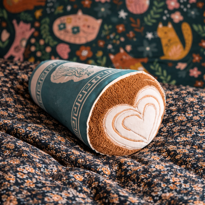 Handmade fabric Greek coffee cup rattle with embroidered latte art, styled on floral fabric with a colorful animal-print background.