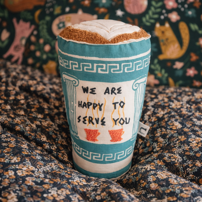 Textile item resembling a coffee cup with decorative design and text on a patterned fabric background