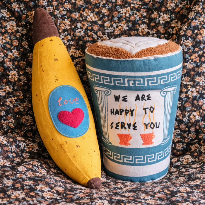 Toy banana and coffee cup pillows on a textured surface