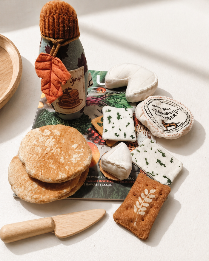 Handmade fabric breakfast play food set with soft pancakes, cheese, crackers, syrup bottle, wooden toy knife and textile deli pieces styled in natural light
