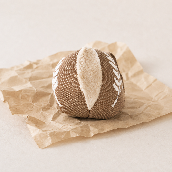 Handmade fabric bread roll toy with a small cosmetic print imperfection, displayed on crumpled brown bakery paper.