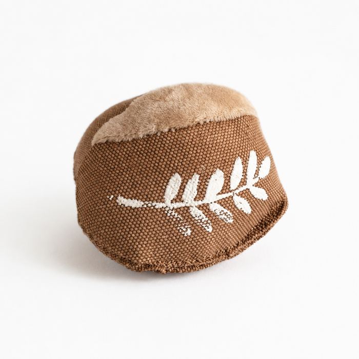 Handmade fabric bread roll toy with a small cosmetic print imperfection, displayed on crumpled brown bakery paper.