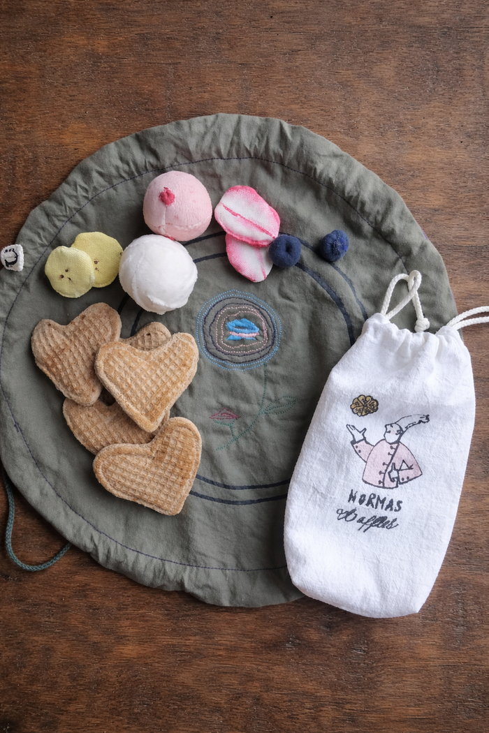 Green drawstring bag with embroidered design, heart-shaped waffles, and a white drawstring pouch on a wooden surface.