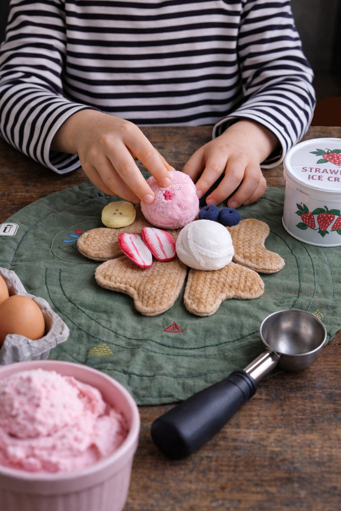 Person decorating fabric heart waffles with fruit and ice on a wooden table.